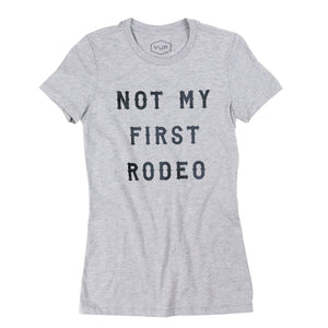 A Ladies cut sarcastic graphic t-shirt in classic Heather Gray, with custom vintage retro typography, reading “Not my first rodeo” — BY fashion brand YUF, from wolfsaint.net