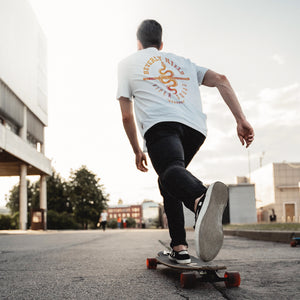 Skateboarder with a long board on the streets, wearing a Retro, vintage-inspired sarcastic fashion t-shirt with a graphic design snake (viper), for a fictional club or gang in Beverly Hills, California. From the brand Ruston/Bond.