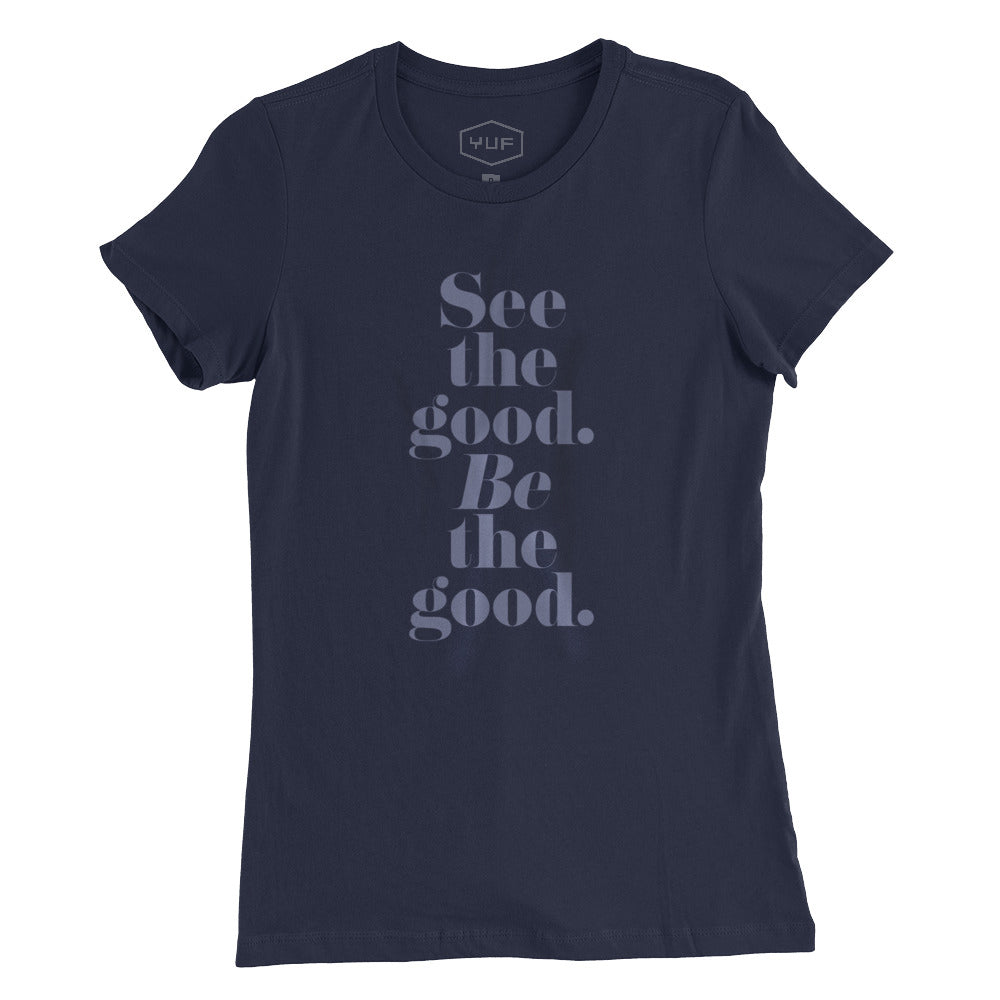 A women’s cut fashion t-shirt in Classic Navy Blue, with elegant typography in a vertical stack: “See the good. BE the good.” By fashion brand YUF, for wolfsaint.net
