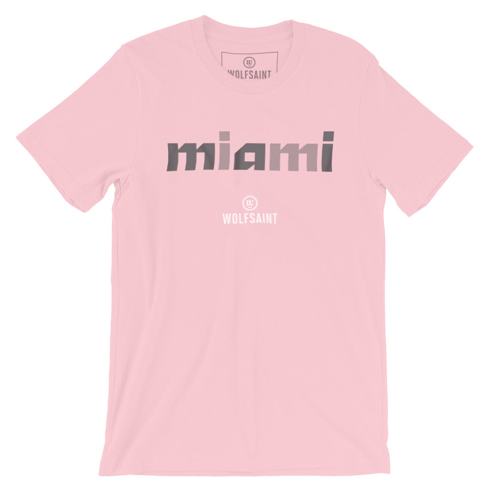 A stylish fashion-shirt in ‘south beach pink,’ with a colorful graphic modern typographic treatment of “miami” in Gray crosshatched lowercase letters, with the Wolfsaint logo beneath it. From wolfsaint.net