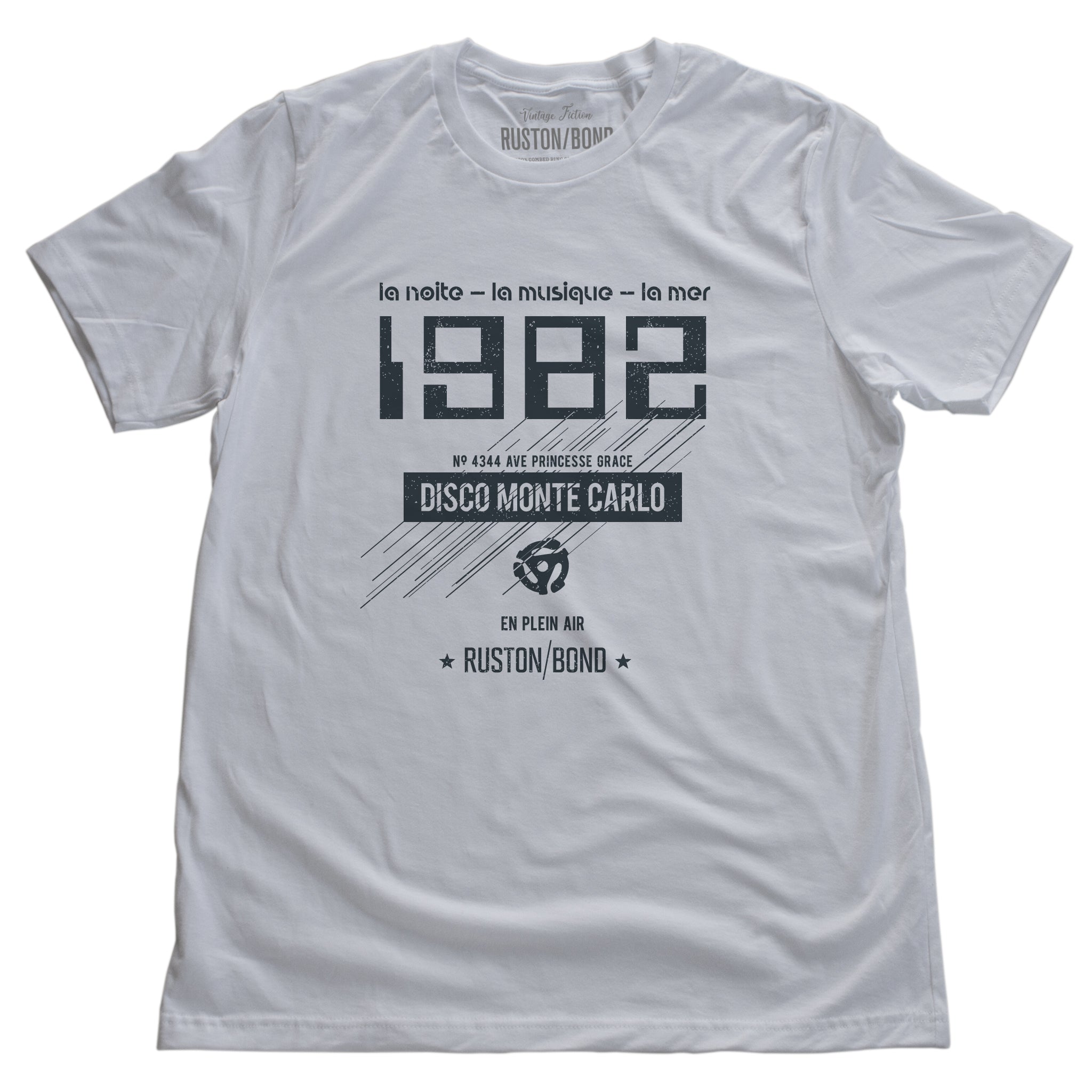 A vintage-inspired t-shirt in white, featuring retro digital font reading “1982” with French taglines and a 45 record adapter graphic, promoting a fictional Monte Carlo discotheque from the 1970s and 80s. By fashion brand Ruston/Bond, from wolfsaint.net