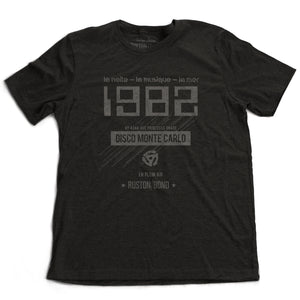 A vintage-inspired t-shirt in classic black, featuring retro digital font reading “1982” with French taglines and a 45 record adapter graphic, promoting a fictional Monte Carlo discotheque from the 1970s and 80s. By fashion brand Ruston/Bond, from wolfsaint.net