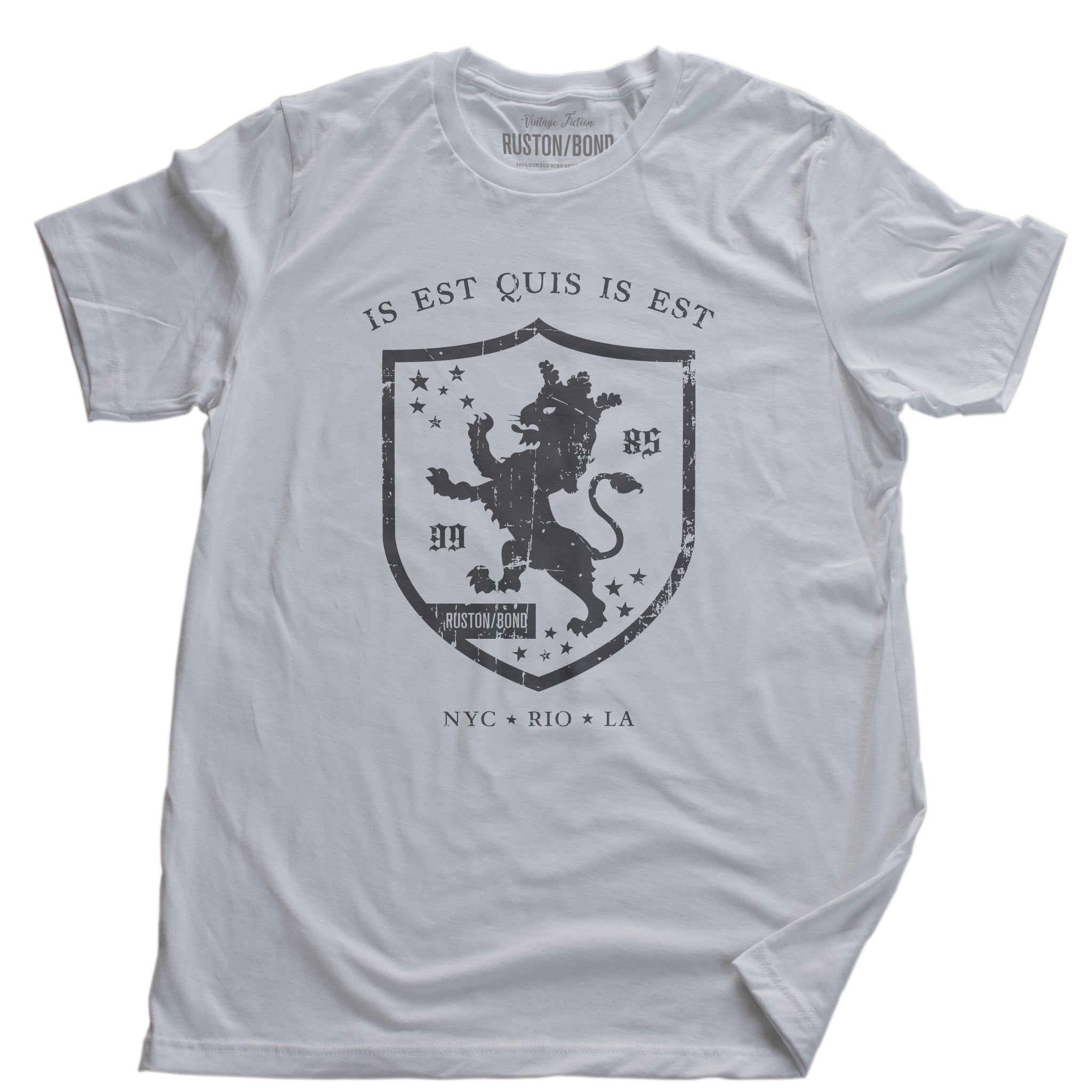 A retro, vintage-inspired fashion t-shirt in Classic White, with an medieval graphic of a lion within a shield,surrounded by the sarcastic text in Latin “it is what it is,” and New York, Rio, Los Angeles at the bottom. By fashion brand Ruston/Bond, from wolfsaint.net