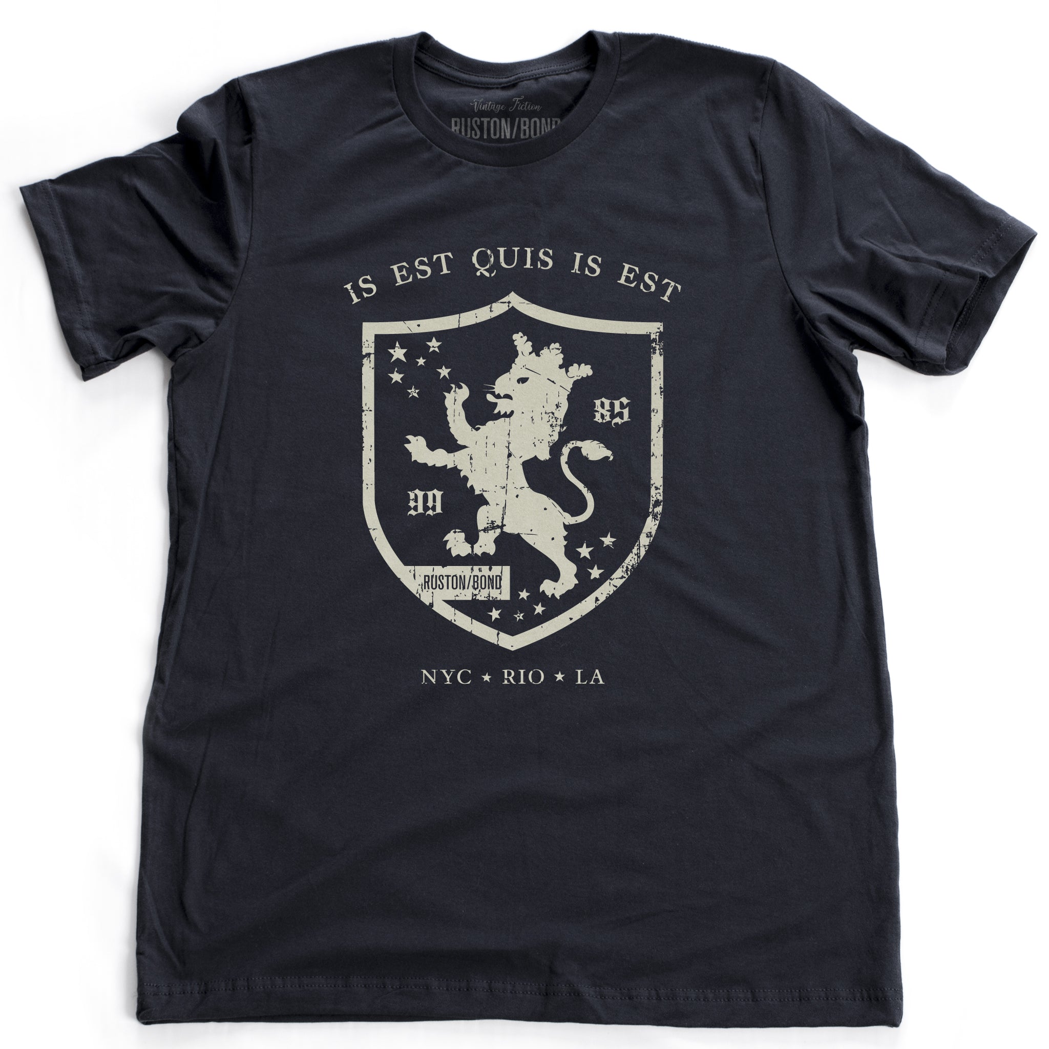 A retro, vintage-inspired fashion t-shirt in classic Navy Blue, with an medieval graphic of a lion within a shield,surrounded by the sarcastic text in Latin “it is what it is,” and New York, Rio, Los Angeles at the bottom. By fashion brand Ruston/Bond, from wolfsaint.net
