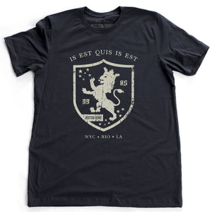 A retro, vintage-inspired fashion t-shirt in classic Navy Blue, with an medieval graphic of a lion within a shield,surrounded by the sarcastic text in Latin “it is what it is,” and New York, Rio, Los Angeles at the bottom. By fashion brand Ruston/Bond, from wolfsaint.net