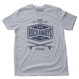 A vintage-inspired, retro design graphic t-shirt with two crossed surfboards below a typographic treatment with the words “SURF ROCKAWAYS FT. TILDEN / New York 1985” by fashion brand Ruston/Bond, for wolfsaint.net