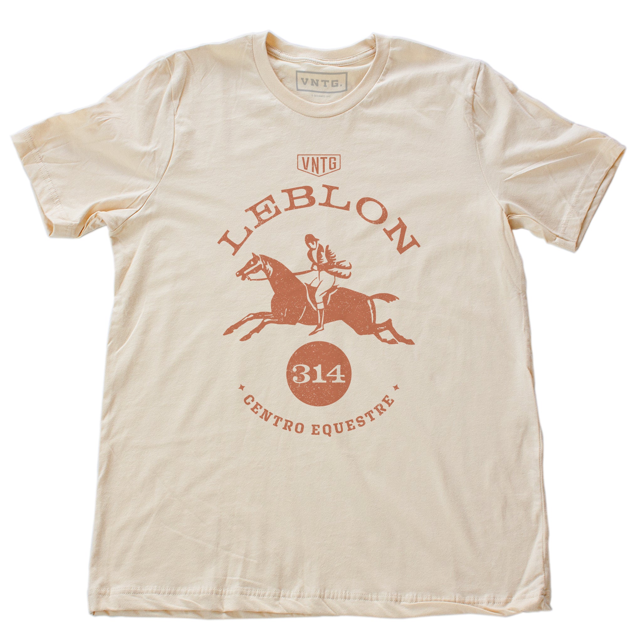 A preppy fashion retro, vintage-inspired t-shirt in Soft Cream, featuring a leaping horse in dressage competition, surrounded by the words “Leblon Centro Equestre” (Leblon Equestrian Center) a fictitious horse training and competition facility in Rio de Janeiro, Brazil. By fashion brand VNTG., for wolfsaint.net