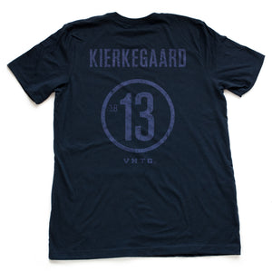 A vintage-inspired retro t-shirt in a mock athletic style, with a sarcastic nod to liberal arts college. This shirt, in Classic Navy Blue features the name of philosopher KIERKEGAARD and his birth year 1813 on the back. By fashion brand VNTG., from wolfsaint.net