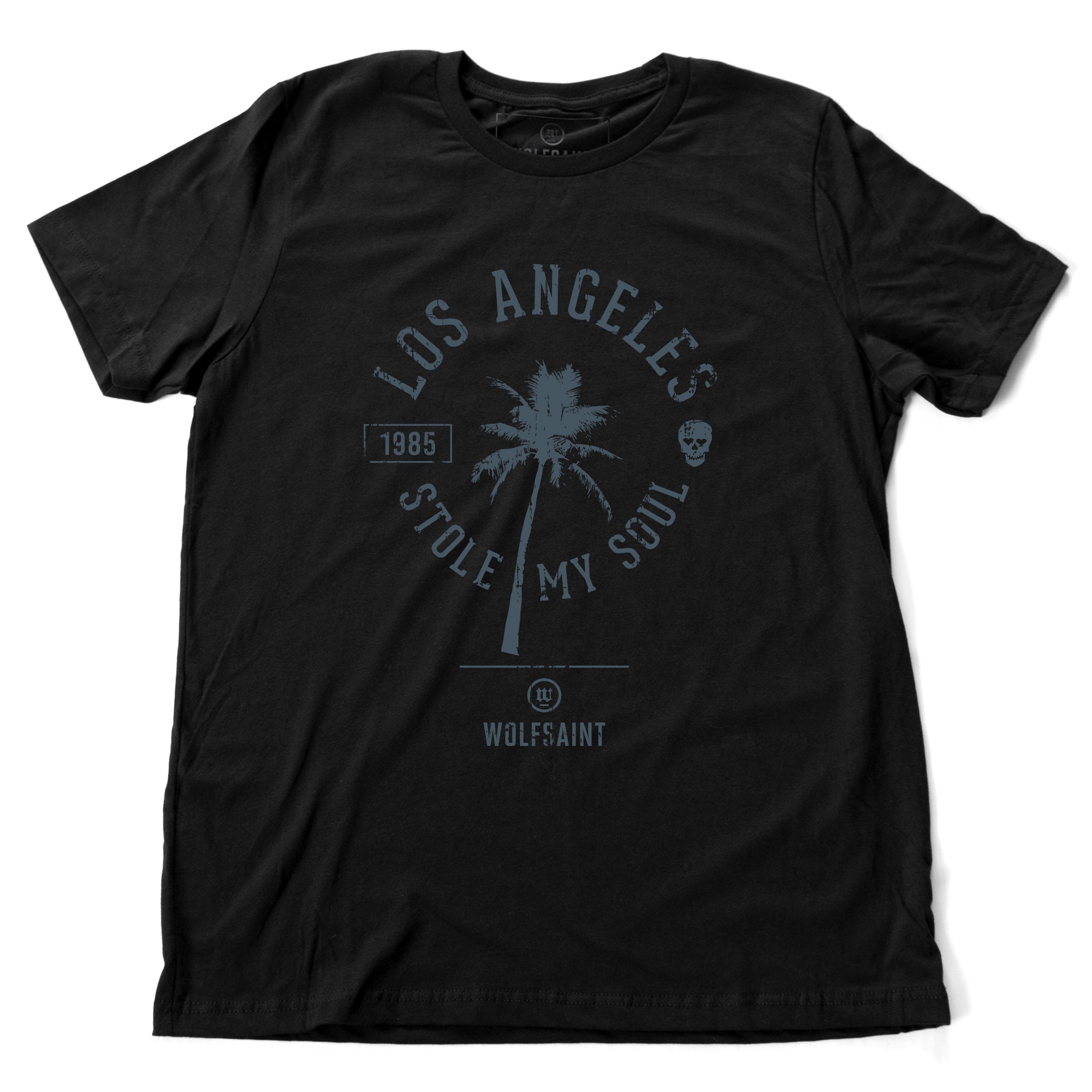 A fashionable retro graphic t-shirt in black, featuring a palm tree surrounded by the sarcastic words “Los Angeles Stole My Soul” with the year 1985 and a fun skull icon. From wolfsaint.net