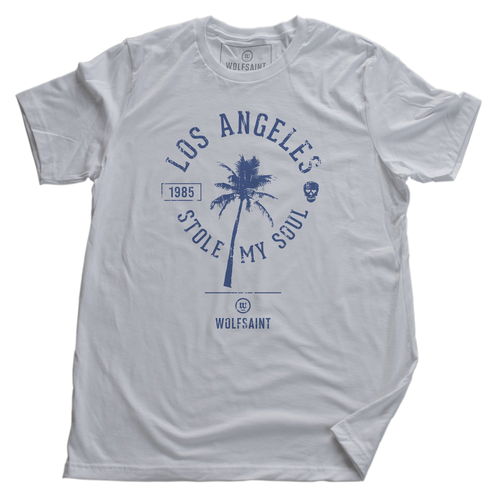 A fashionable retro graphic t-shirt in white, featuring a palm tree surrounded by the sarcastic words “Los Angeles Stole My Soul” with the year 1985 and a fun skull icon. From wolfsaint.net