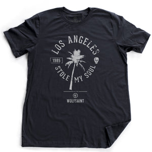 A fashionable retro graphic t-shirt in Classic Navy Blue, featuring a palm tree surrounded by the sarcastic words “Los Angeles Stole My Soul” with the year 1985 and a fun skull icon. From wolfsaint.net