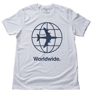 The front of the white version of a fashion t-shirt representing a jetsetting lifestyle. On the front of the shirts is a simple graphic of a commercial airliner superimposed on a globe, and the word “Worldwide.” On the reverse is a stack of airport codes representing international travel (New York/JFK, Los Angeles/LAX; Rio de Janeiro/GIG; San Jose Costa Rica/SJO; Tokyo/NRT; Paris/CDG). By fashion brand WOLFSAINT, from wolfsaint.net