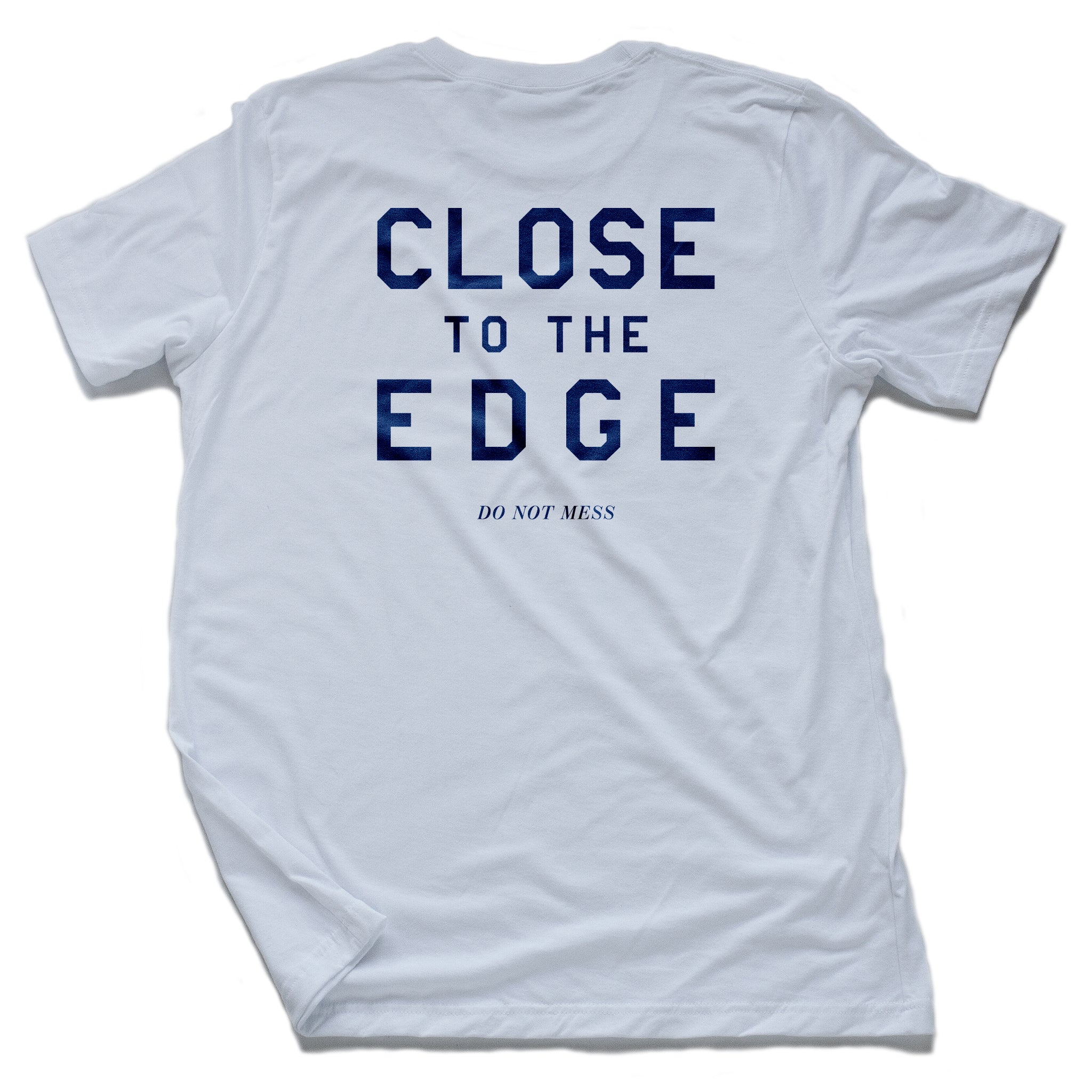 A bold graphic t-shirt in white, with classic, retro typography “CLOSE TO THE EDGE” on the back. By the fashion brand YUF,  From wolfsaint.net