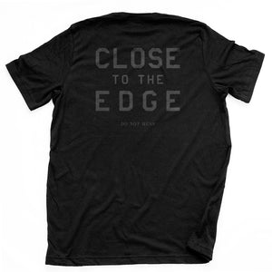 A bold graphic t-shirt in black, with classic, retro typography “CLOSE TO THE EDGE” on the back. By the fashion brand YUF,  From wolfsaint.net