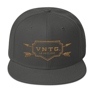 A classic SnapBack cap in Gray, featuring the VNTG. logo and it’s cities (Los Angeles, New York City, Rio de Janeiro) within a shield, edged with crossing arrows. From wolfsaint.net