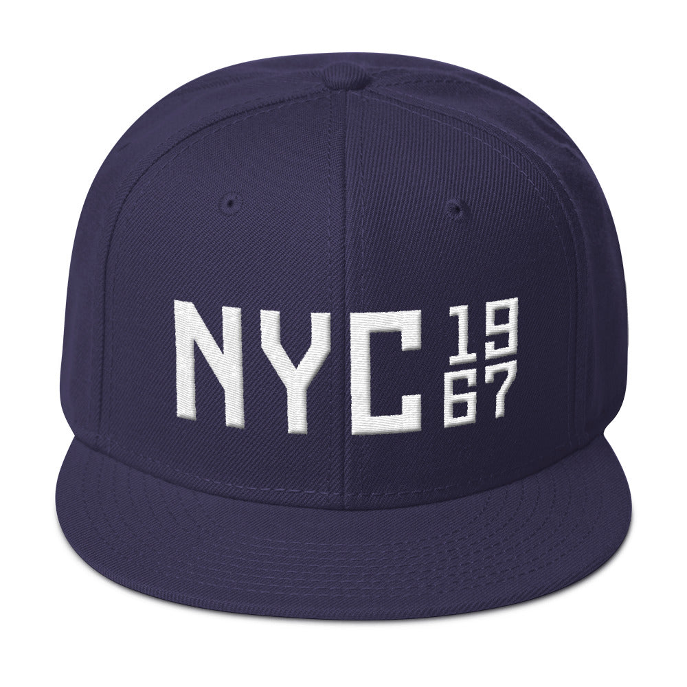 A puff embroidery high-profile SnapBack cap in Navy Blue, with white thread of a large “NYC” (New York City) with the vintage year 1967 in a stack to the side. From wolfsaint.net 