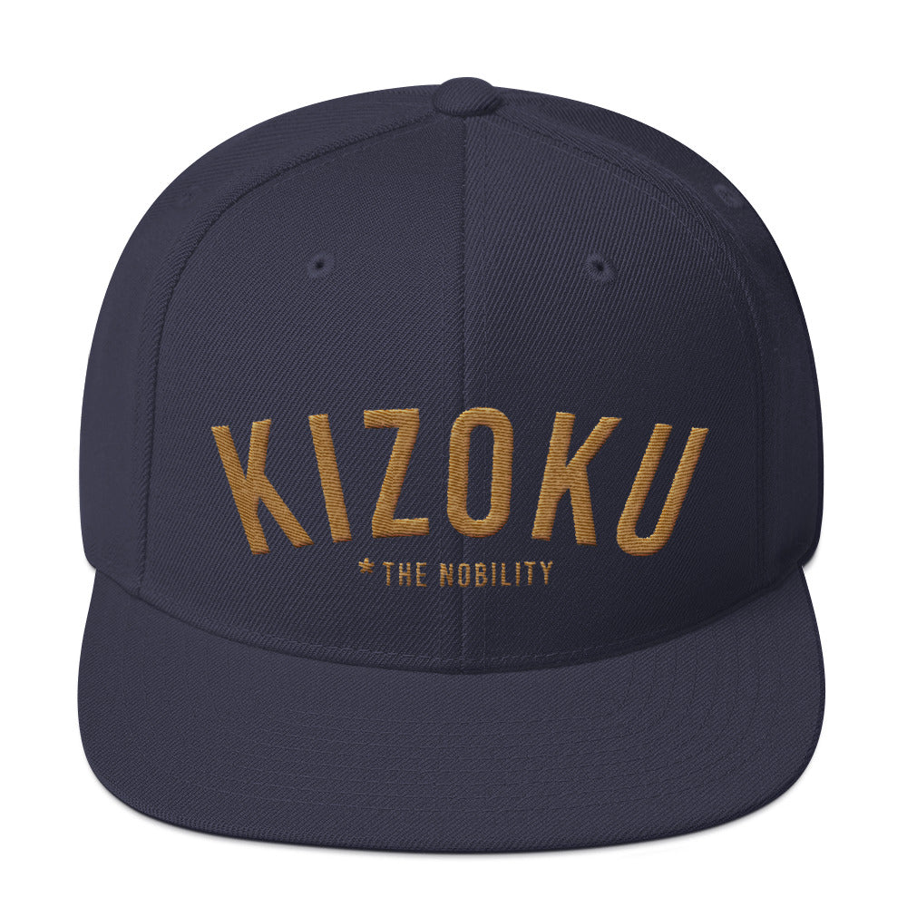 A classic SnapBack cap in Navy Blue, with the Japanese word “KIZOKU” in raised gold embroidery, representing “The Nobility” —by fashion brand WOLFSAINT, from wolfsaint.net